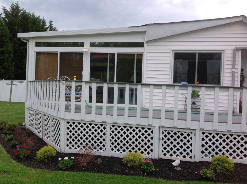 White house with a screened porch and raised deck above a flower-lined lawn.
