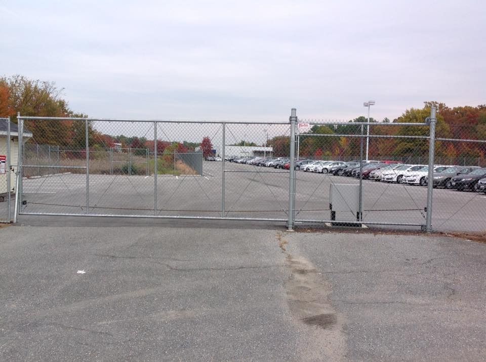 Chain-link gate blocking an empty parking lot with parked cars in the distance