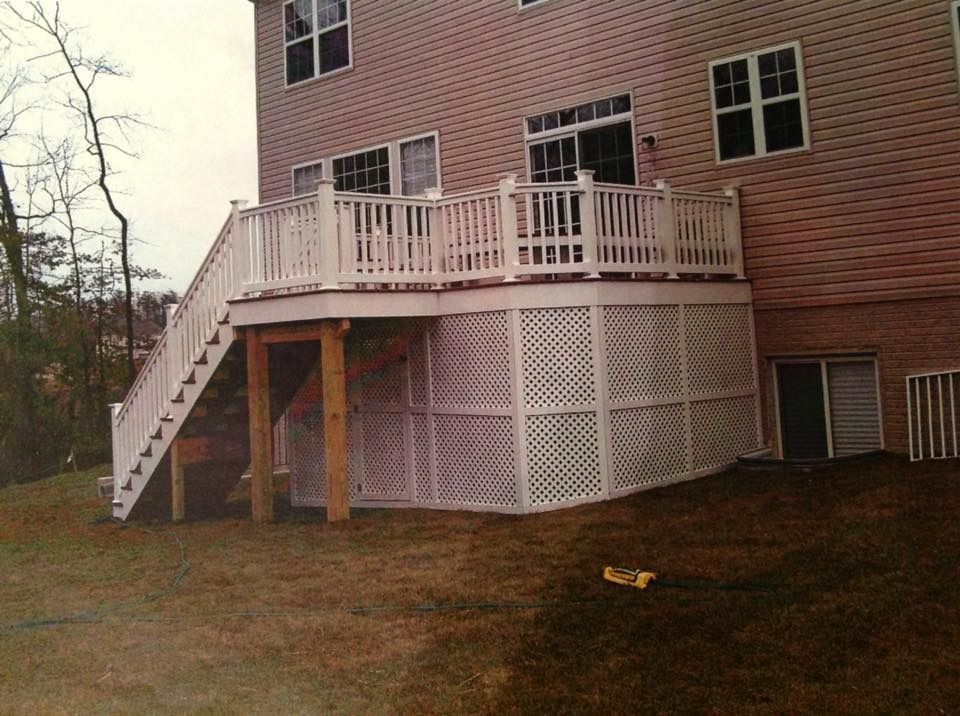 Brick house deck with white railing and stairs, and lattice skirting over a sloped yard