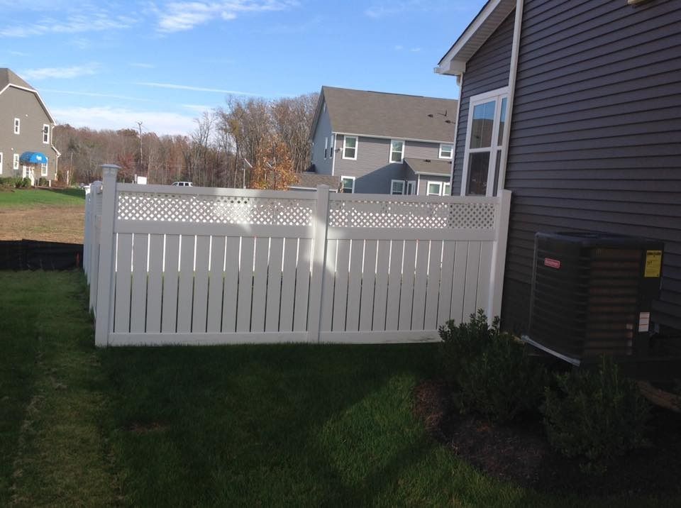 White vinyl fence in a suburban backyard beside a house on a sunny day.