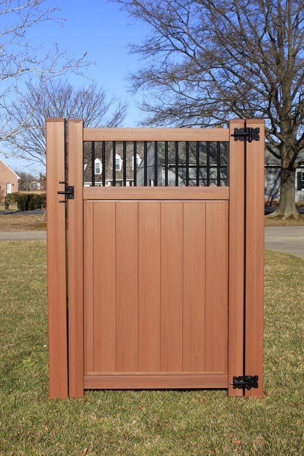 Closed wooden gate with black hinges and a small barred window, outdoors on a lawn with trees behind.