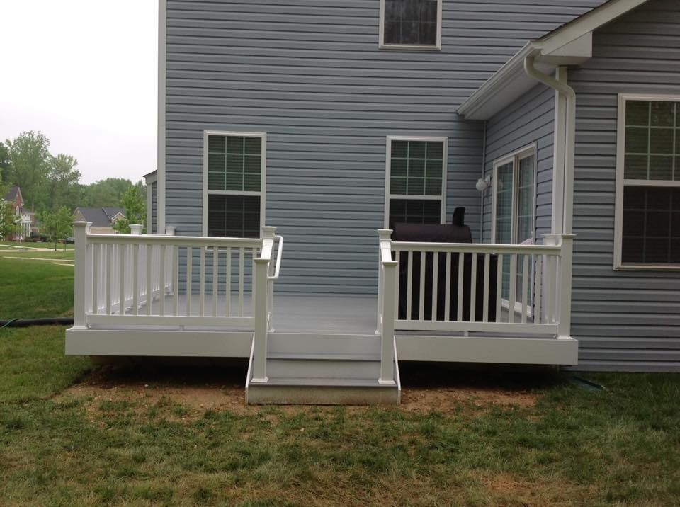 Rear deck with white railings and stairs on a gray house, with a person standing on the right side patio.