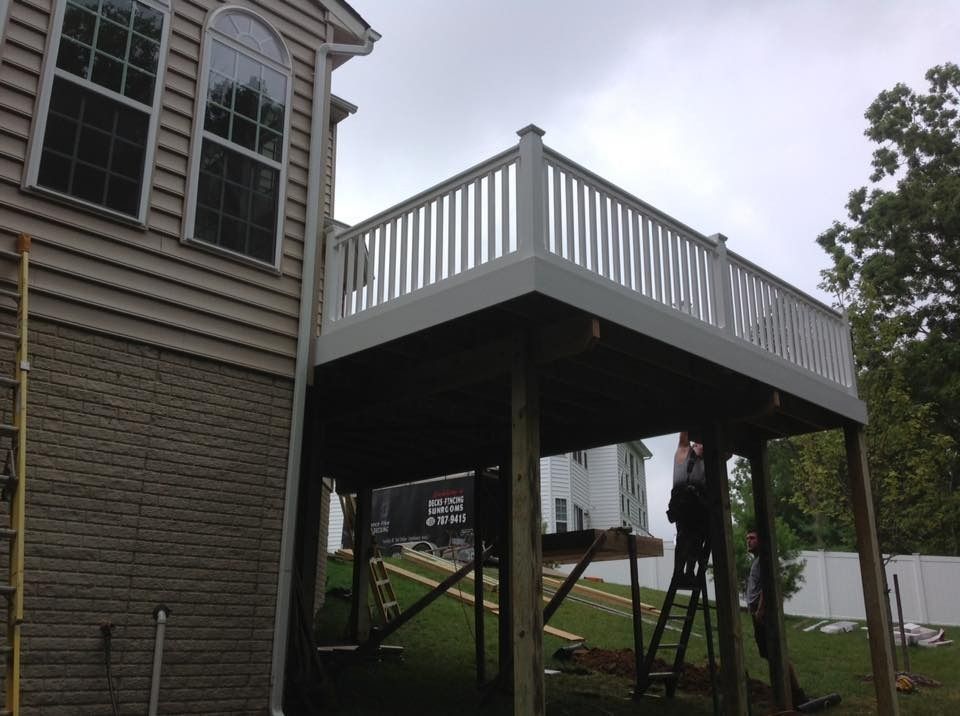 House exterior with a raised deck under construction, white railing on a gray siding home.