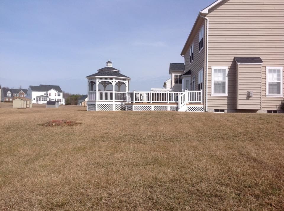 Suburban houses with a white gazebo and fenced deck beside a dry grassy lot