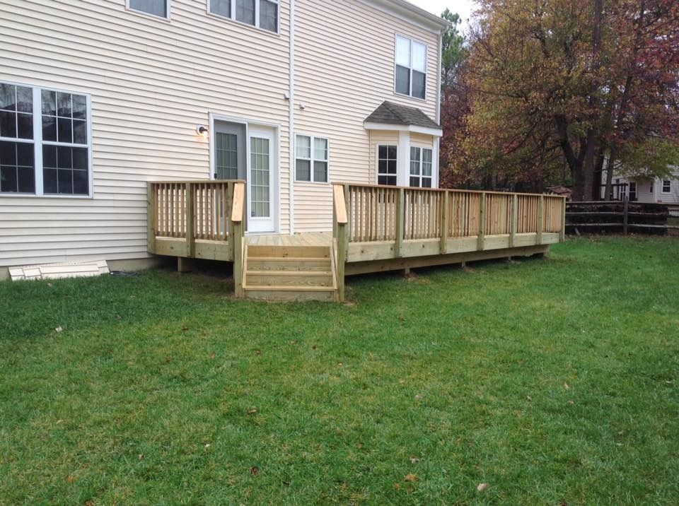 Wooden deck and ramp attached to a beige house, overlooking a grassy yard.