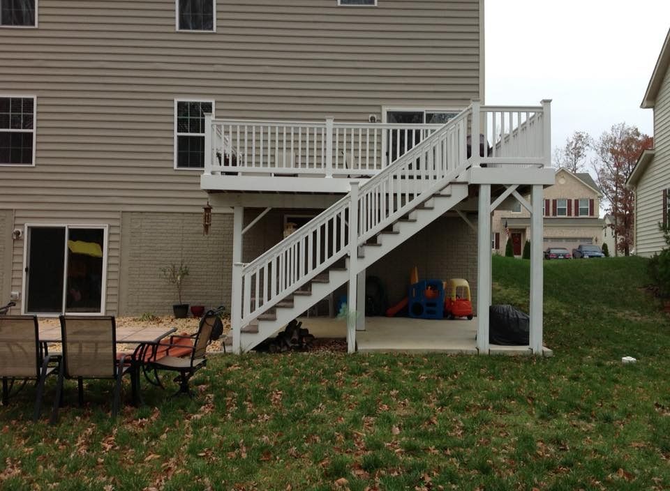 Backyard deck with white railing and stairs attached to a beige house, with patio furniture below
