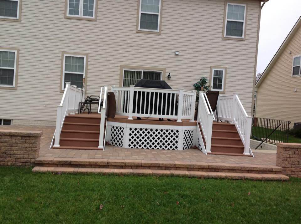 Back deck with white railings, red steps, and a black grill against a beige house.
