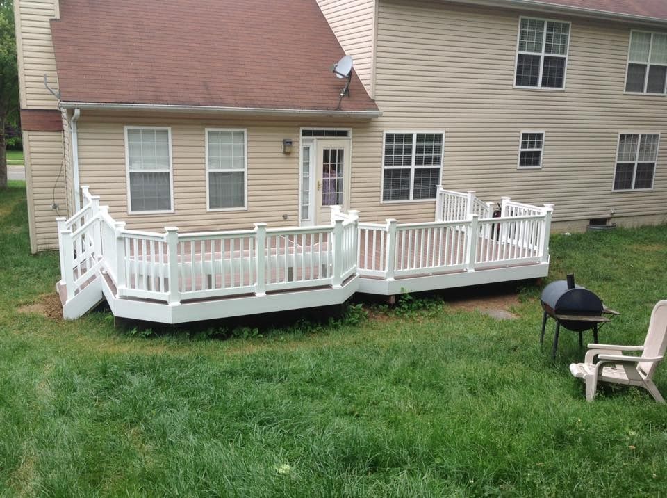 Backyard deck with white railing beside a beige house, overlooking a grassy yard and a grill