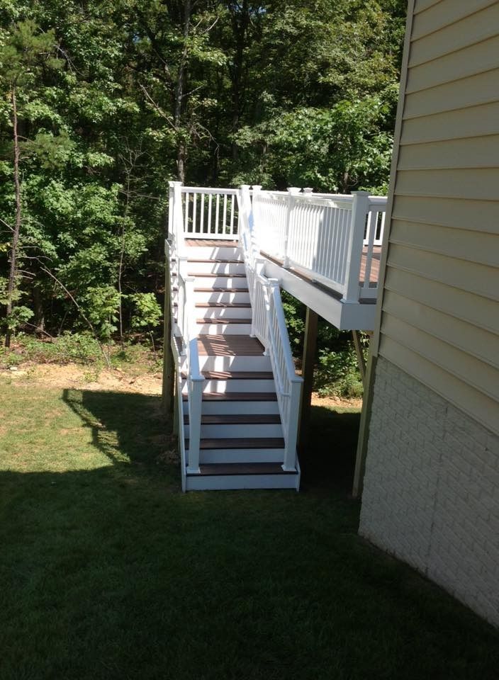 White outdoor staircase and deck beside a house, set in a grassy yard with trees in the background.