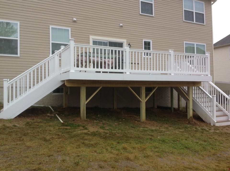 Back deck and stairs on a beige house, with white railings and posts over a grassy yard