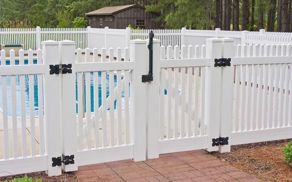 White vinyl fence around a blue swimming pool in an outdoor backyard setting