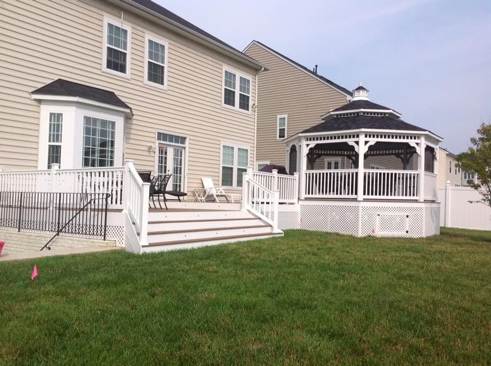 Backyard deck with white railings, steps, and a gazebo beside a beige house.