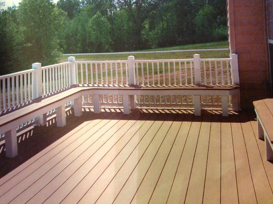 Sunlit wooden deck with white railing and bench seating beside a brick wall