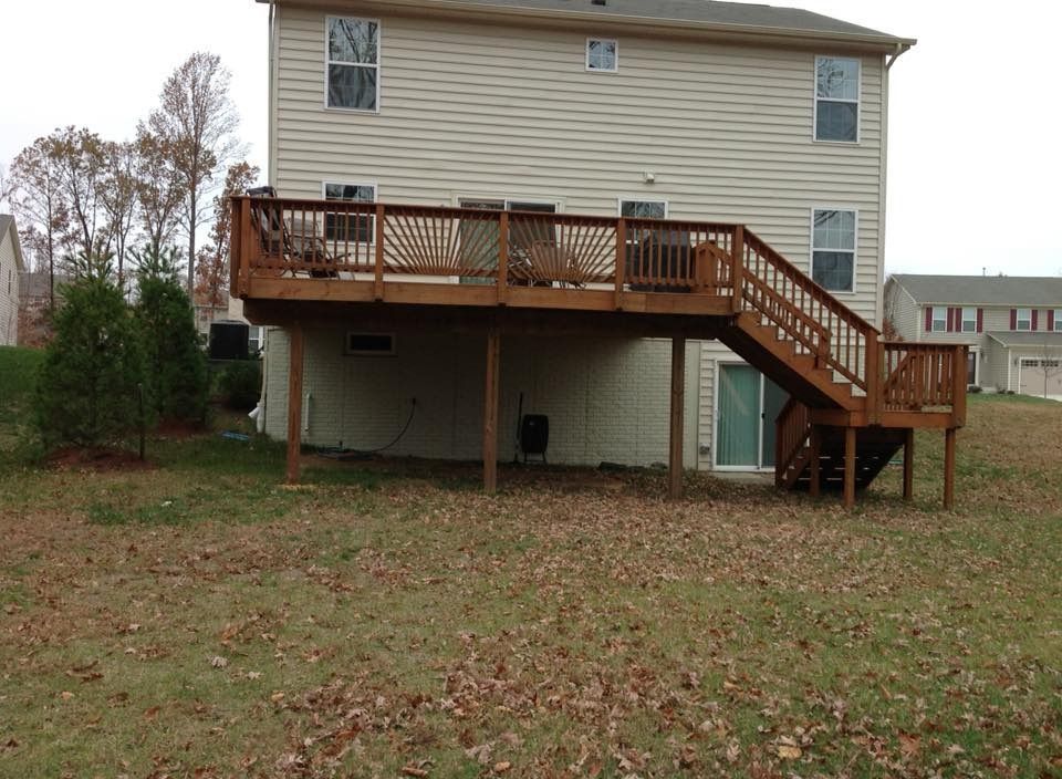 Raised wooden deck with stairs on the back of a beige house in a grassy yard