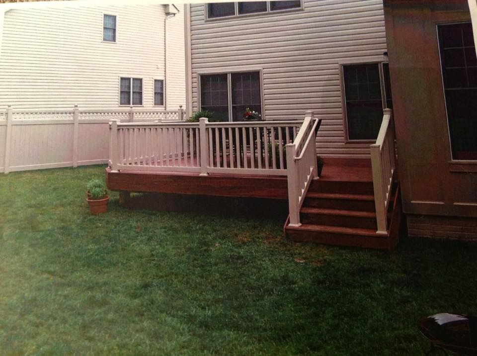 Back deck with wooden stairs, white railing, and a grassy yard beside a house.
