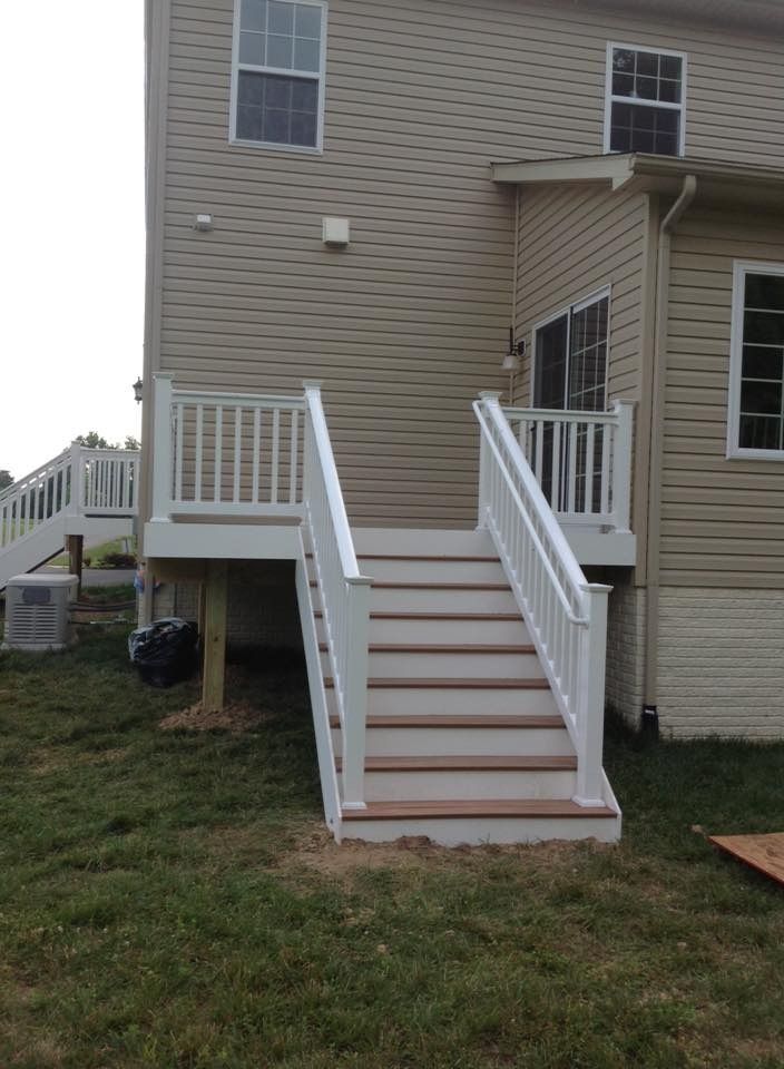 Exterior stairs with white railings leading to a second-story deck on a beige house.