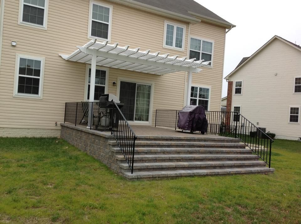 Backyard patio with steps, black railings, grill, and a covered patio against a beige house