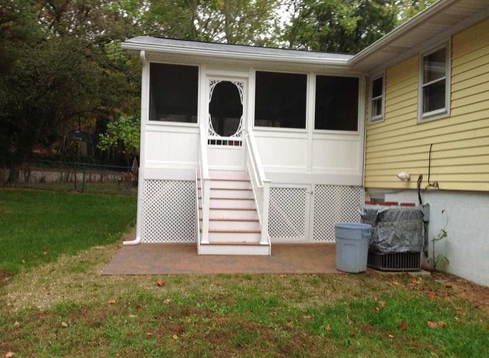 Back porch with white screened entry and stairs on a yellow house, grassy yard in front