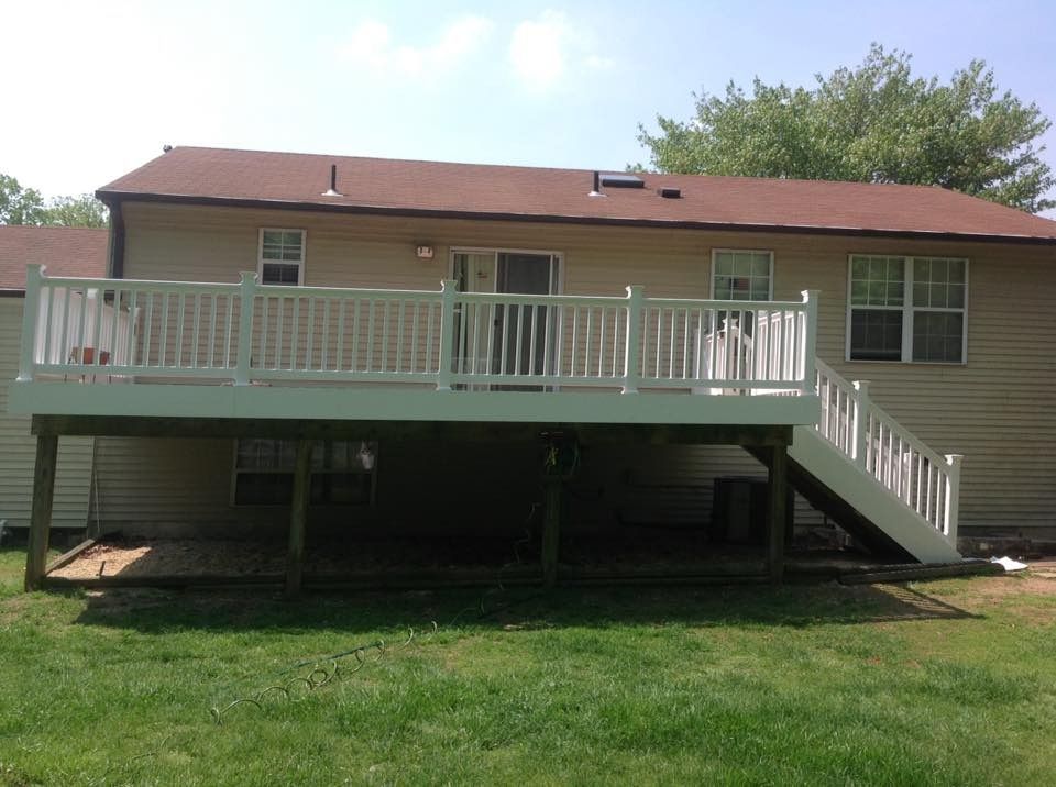 Single-story beige house with a raised wooden deck and staircase, viewed from the backyard.
