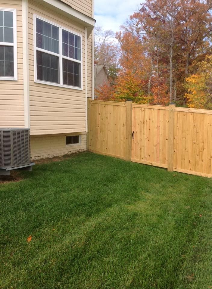 Backyard beside beige house with green lawn, wooden fence, and autumn trees in the background