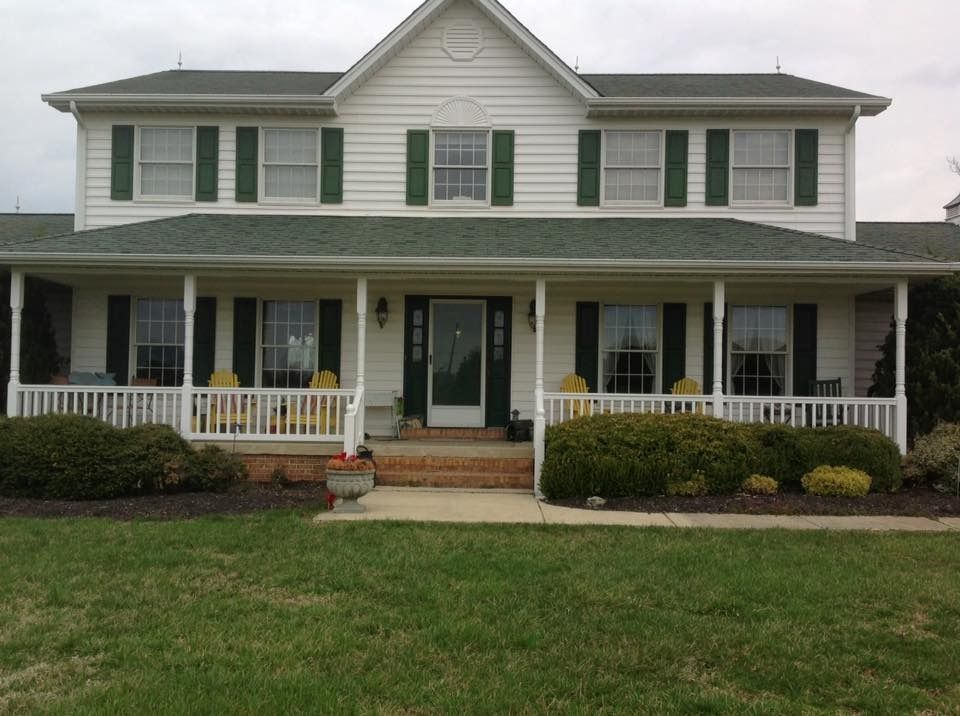 Two-story white house with green shutters, front porch, and a manicured lawn.