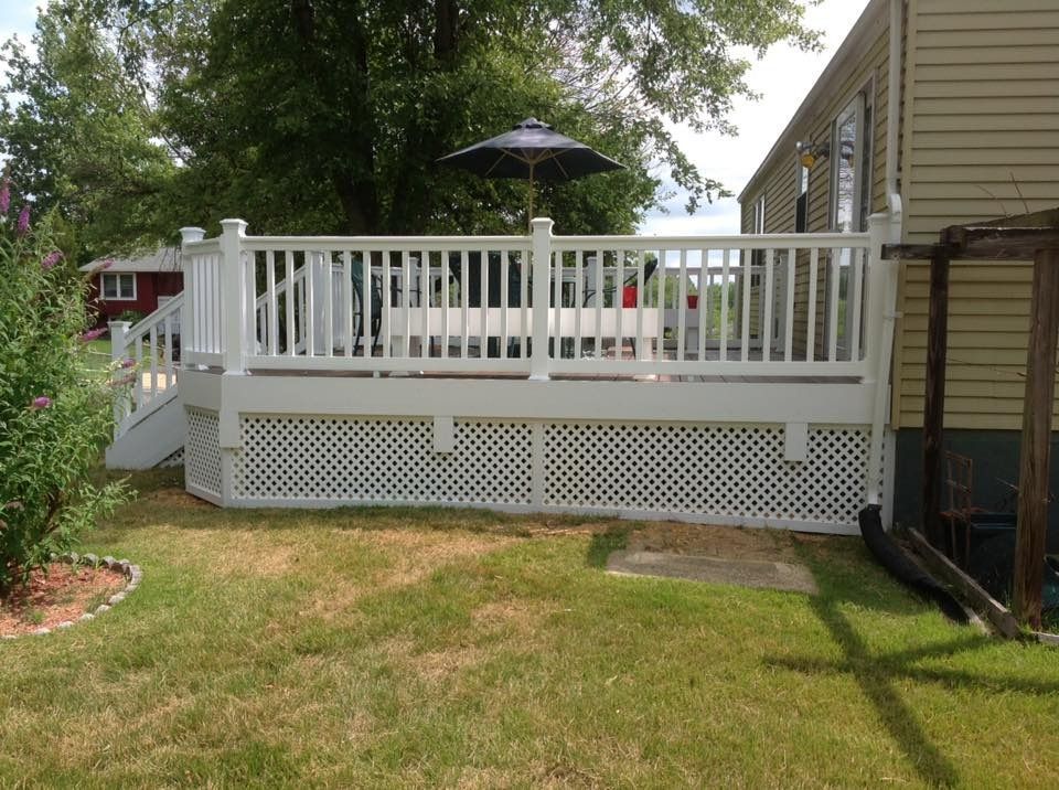 White deck with railing and umbrella beside a house in a backyard with grass and trees