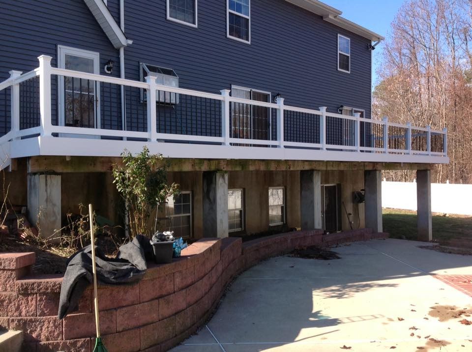 House exterior with elevated deck and white railing over a brick retaining wall, seen from the driveway