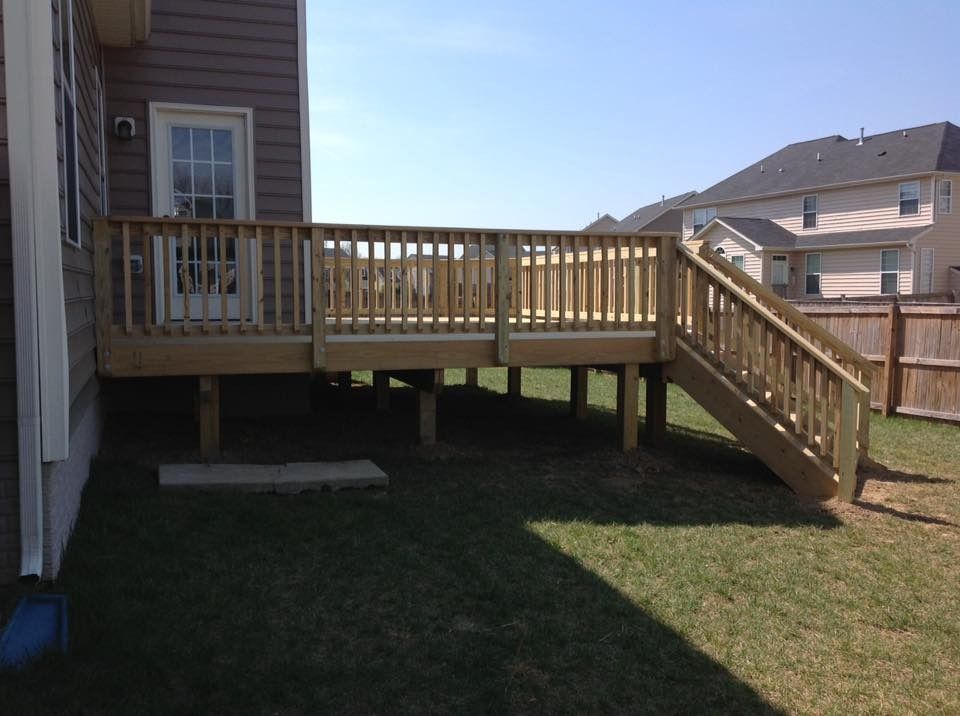 Wooden backyard deck with stairs beside a house on a grassy lawn