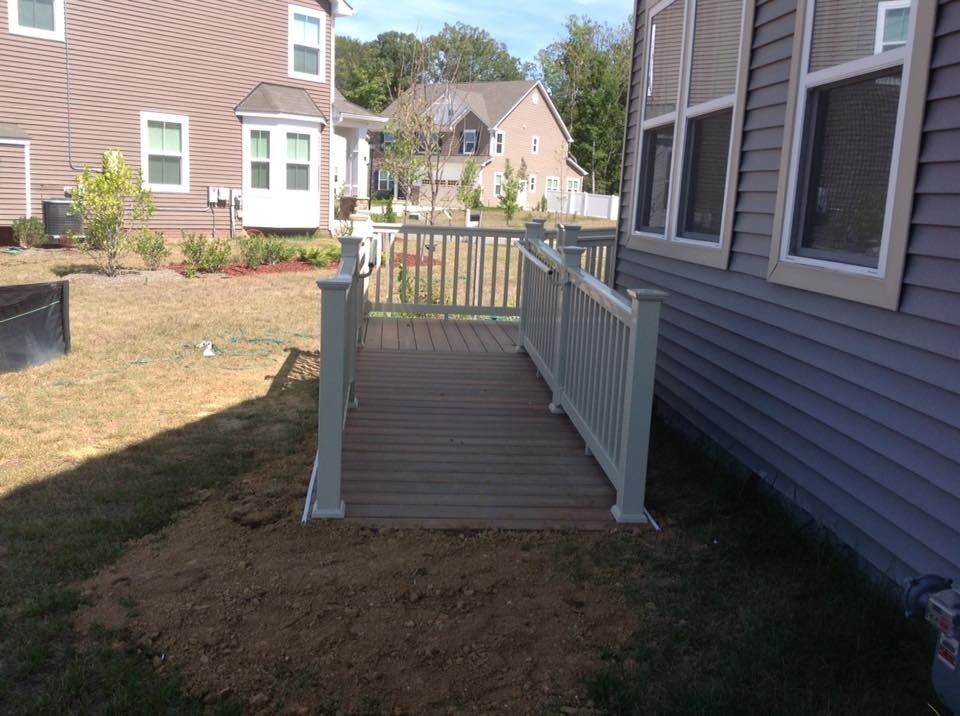 Backyard wooden ramp with white railings beside a house, leading to a fenced deck area.
