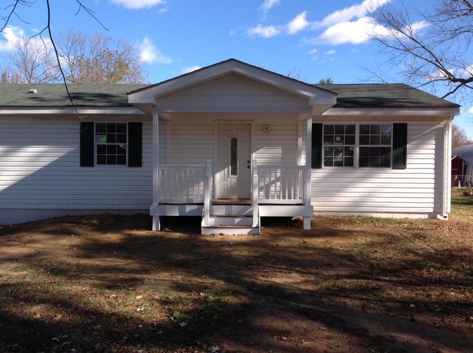 Small white house with a centered front porch, black shutters, and a grassy yard under a blue sky