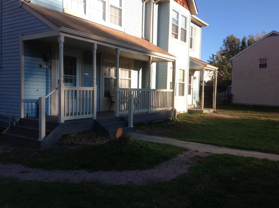 White two-story house with a front porch, blue siding, and a grassy yard in daylight