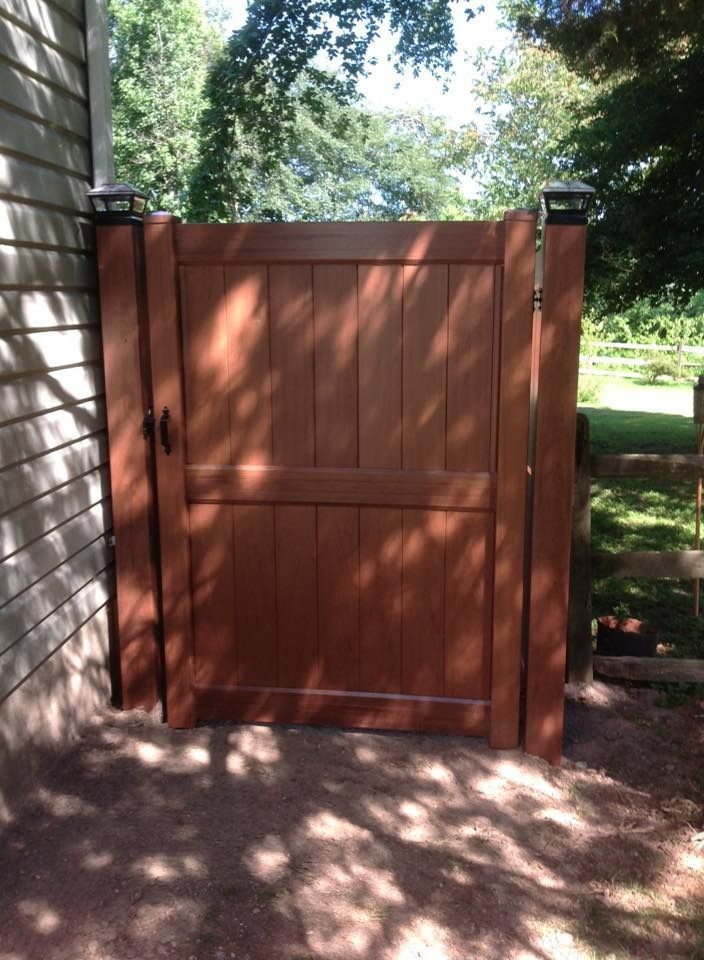 Wooden backyard gate with a latch, framed by trees and dappled sunlight.