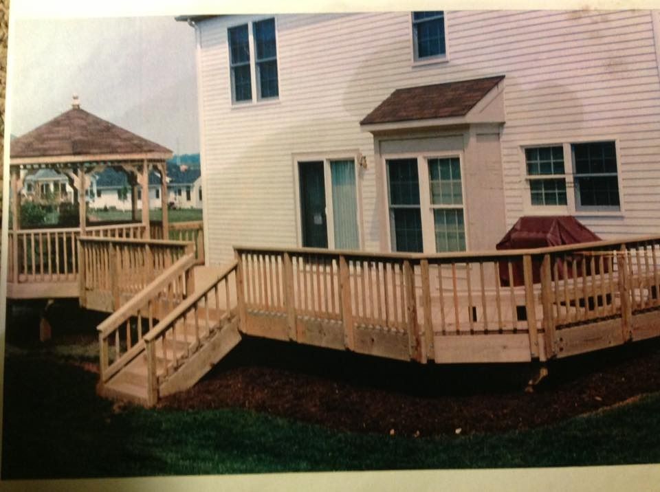Wooden deck and ramp around a beige house, with a gazebo on the left and a red covered grill on the right
