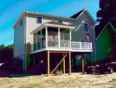 Elevated house with a white porch and support beams on a sunny day, set on a hillside