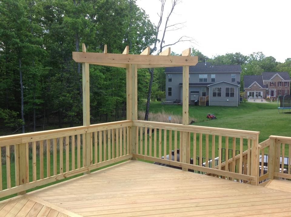 Wooden deck with railing and pergola posts overlooking suburban homes and a grassy yard