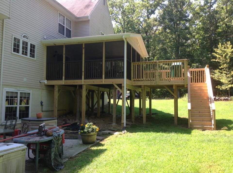 Raised wooden deck with screened porch and stairs beside a beige house in a sunny backyard