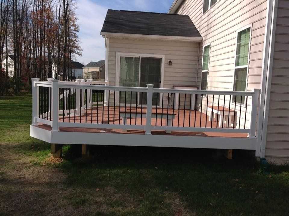 Back deck with white railing attached to a beige house, with sliding glass doors and potted plants on the deck.
