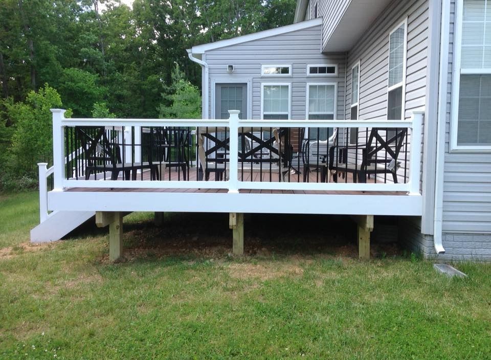 White backyard deck with black railing, outdoor table and chairs beside a gray house.