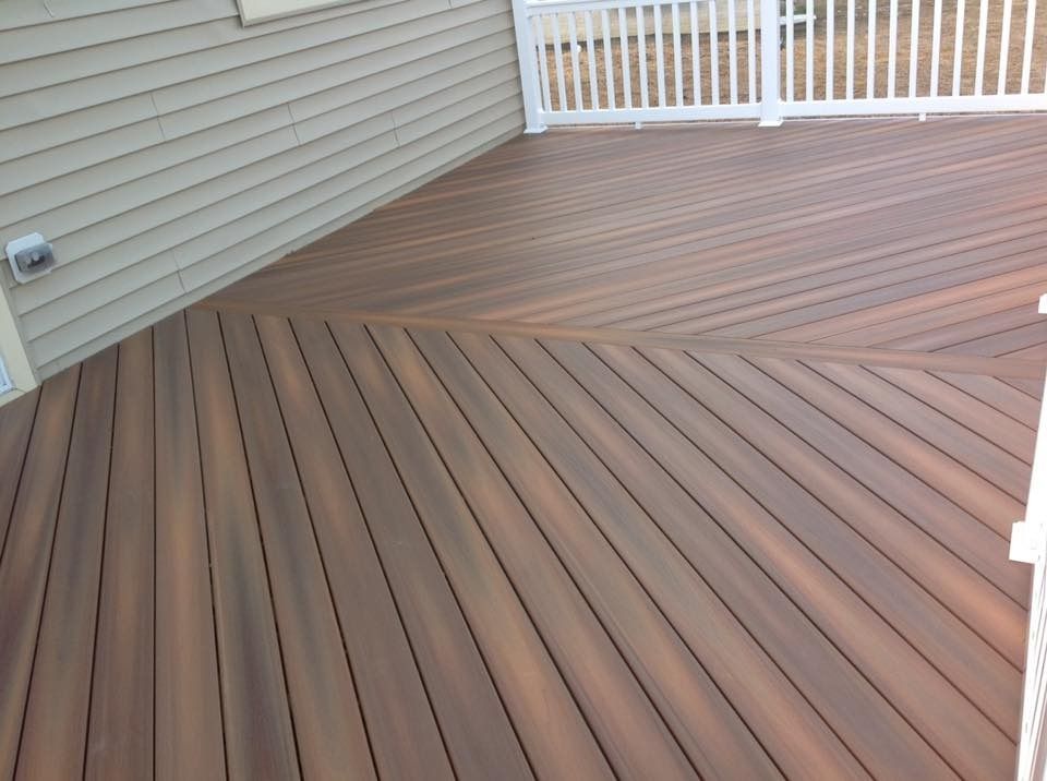 Wooden deck with diagonal and straight brown planks beside beige house siding and white railing.