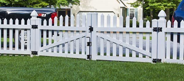 White picket fence with a double gate in front of a house and green lawn