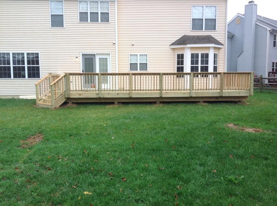 Backyard with wooden deck and stairs attached to a beige house, overlooking a grassy lawn.