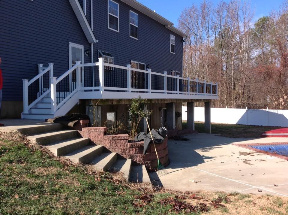 House with raised deck, stairs, and patio in a wooded backyard on a sunny day