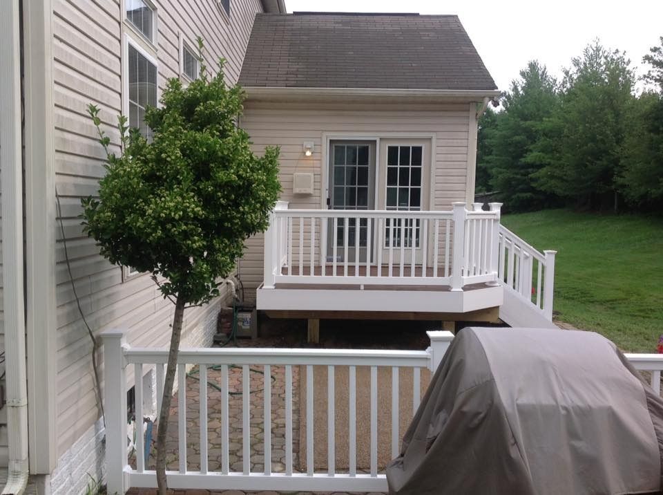 Backyard deck with white railing, small balcony, potted tree, and a covered grill beside a house