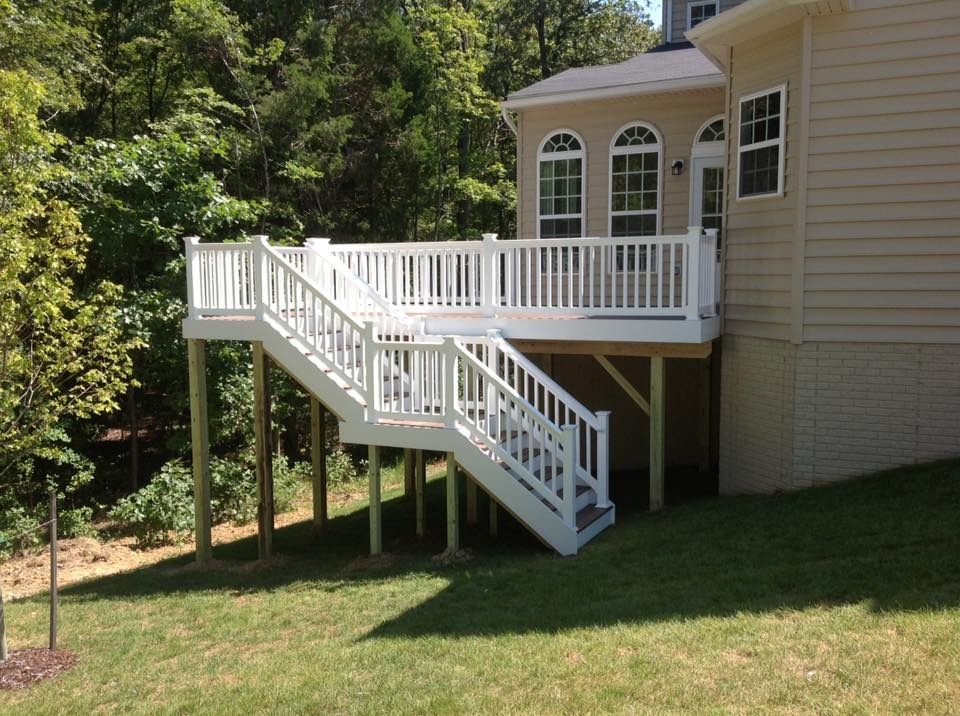 White wooden deck and stairs attached to a beige house in a wooded yard