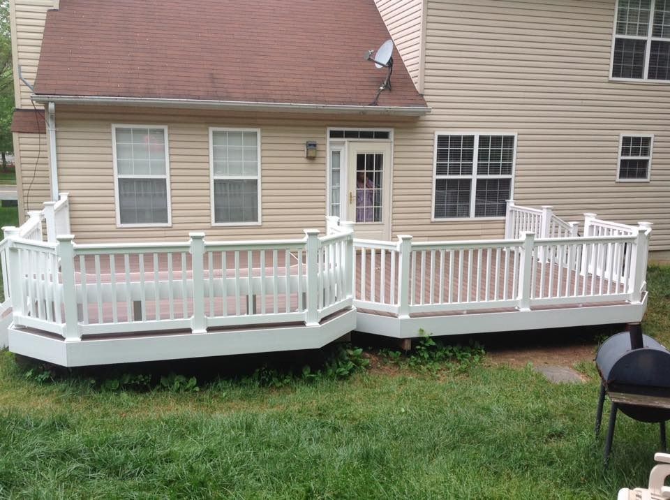White wooden deck with railings attached to a beige house, beside a grassy yard