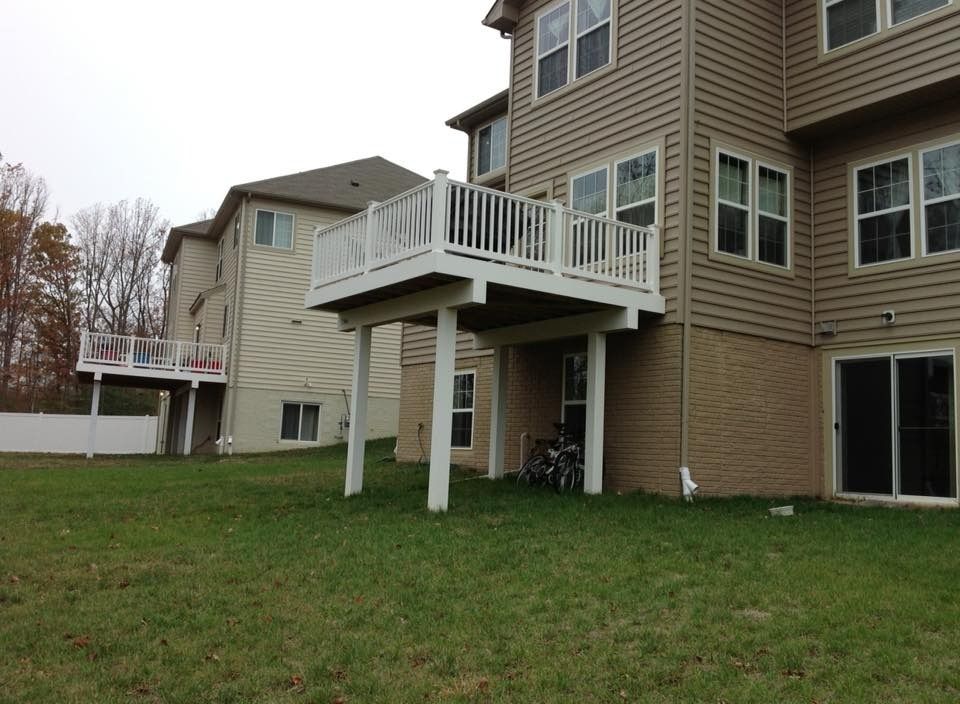 Back of a tan house with a raised deck, white railings, and a grassy yard