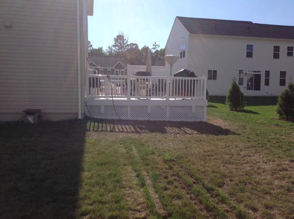 Backyard with white wooden deck attached to a house, overlooking a grassy lawn and neighboring homes.