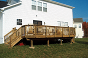 White house with a wooden raised deck and stairs in a grassy backyard