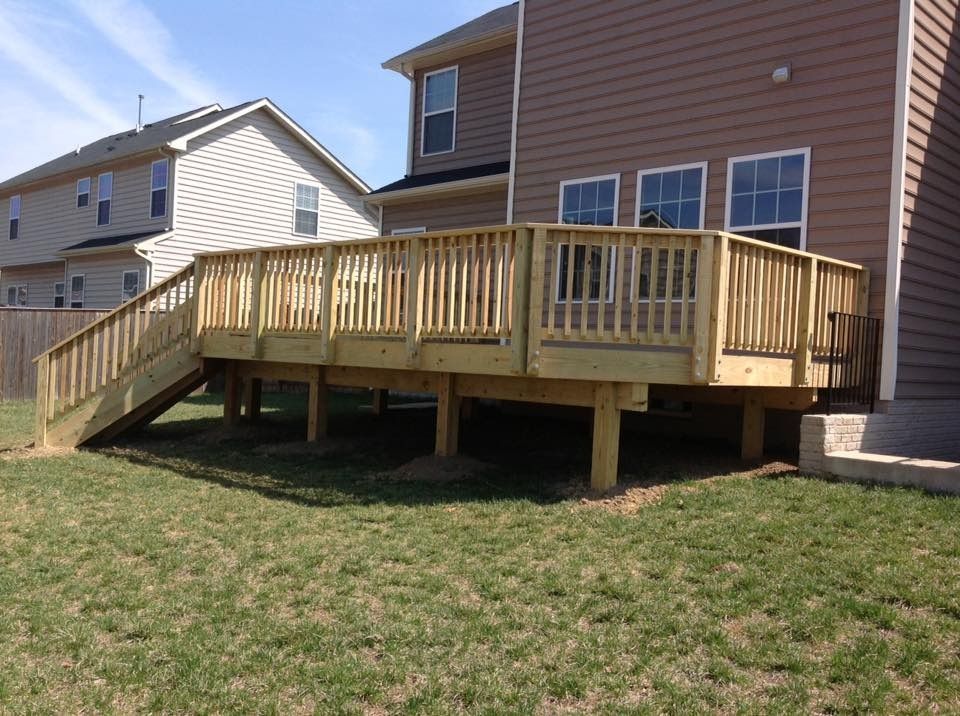 Wooden backyard deck with railing and stairs attached to a house on a grassy lawn