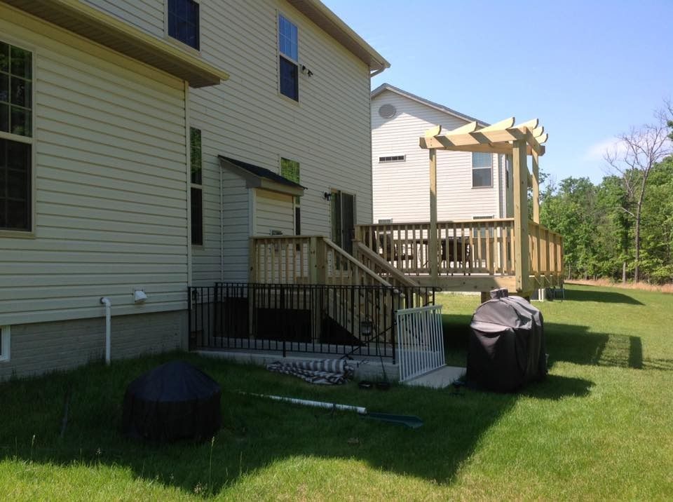 Backyard with a beige house, wooden deck, grill, and green lawn on a sunny day
